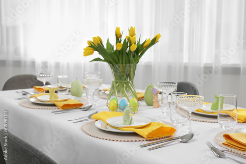 Festive table setting with glasses, painted eggs and vase of tulips. Easter celebration