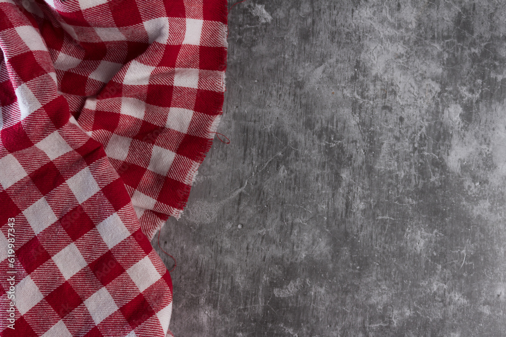 Fototapeta premium Concrete table with red and white checkered tablecloth, seen from above.