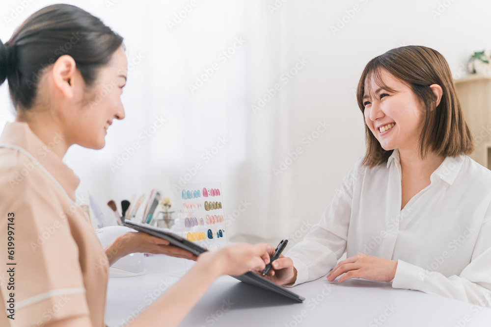 ネイルサロンでタブレットの契約書に電子サインするカウンセラースタッフと相談する日本人女性
