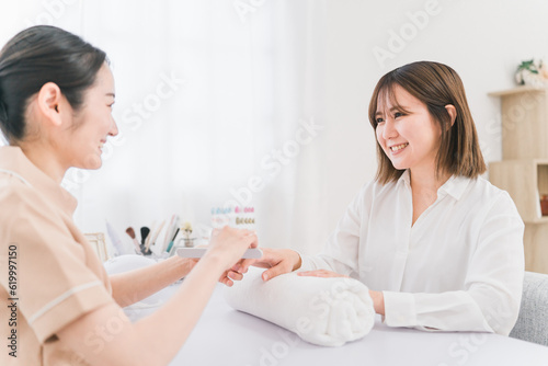 ネイルサロンでサンディングするネイリストと施術を受ける日本人女性 