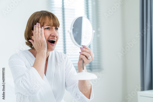 Caucasian senior woman looking at mirror after apply lotion on face. 