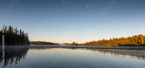 a small moon in a clear blue morning sky over a lake in Ontario Canada
