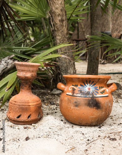 Hand made ceramic pot in sandy tropical garden with green palm leaves on a sunny day in Tulum  photo