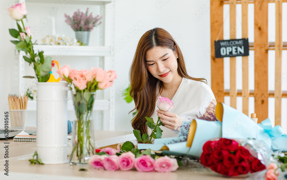 Portrait shot of Asian professional successful beautiful female florist designer flower shop owner entrepreneur decorating pink roses bouquet vase in floral garden store studio