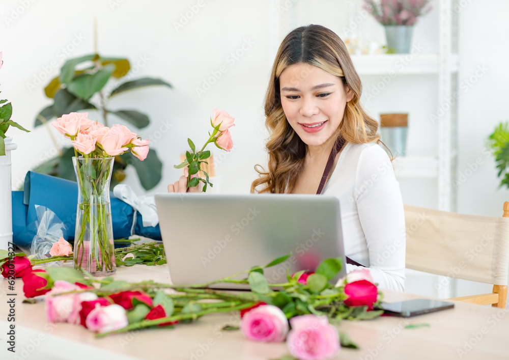 Asian happy cheerful professional successful female florist designer shop owner entrepreneur businesswoman in apron sitting working stock using laptop notebook computer in floral garden store studio