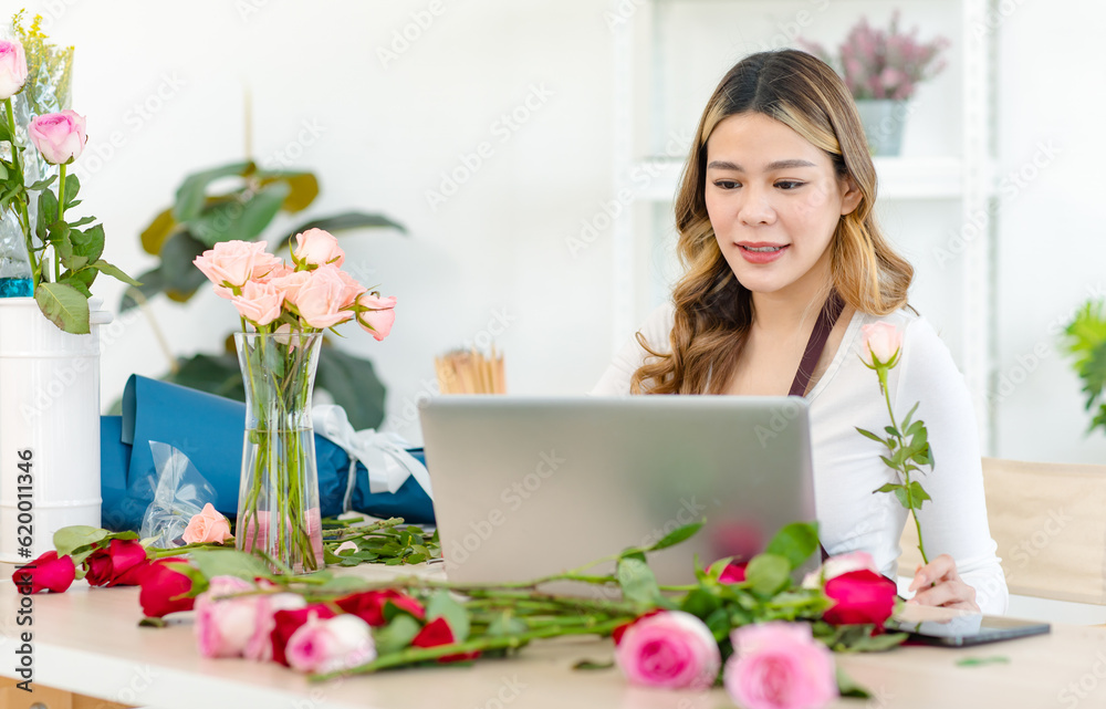 Asian happy cheerful professional successful female florist designer shop owner entrepreneur businesswoman in apron sitting working stock using laptop notebook computer in floral garden store studio