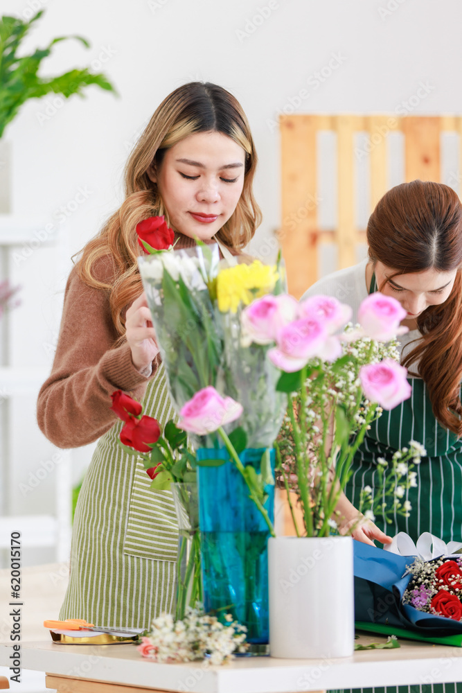 Asian professional successful female florist designer flower shop owner entrepreneur and colleague employee helping decorating flower bouquet in vase in floral garden store studio.