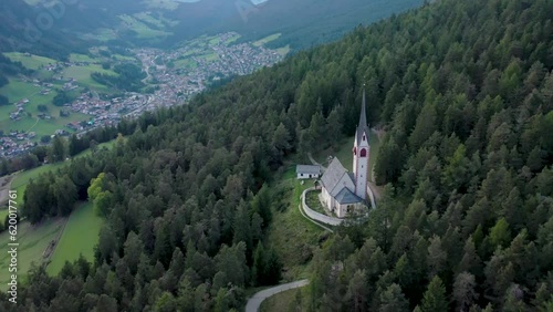 Aerial drone view of an old secluded mountain top church in the Italian alps surrounded by a forrest of trees 05