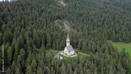 Aerial drone view of an old secluded mountain top church in the Italian alps surrounded by a forrest of trees 02