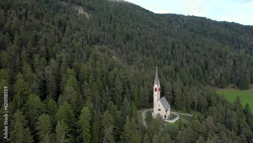 Aerial drone view of an old secluded mountain top church in the Italian alps surrounded by a forrest of trees 01