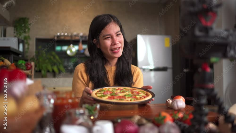 Asian beautiful woman baking a pizza and making a video live streaming on social network. Asian beautiful woman baking a pizza and making a video live streaming on social network.