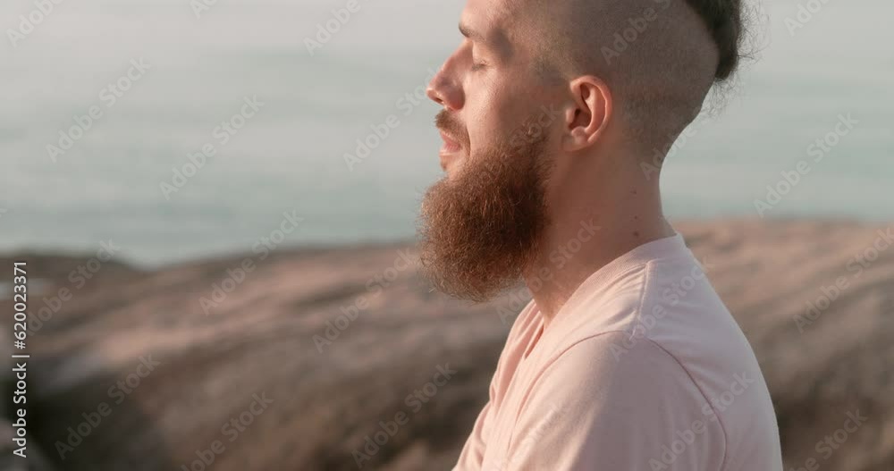 Close-up portrait of enlightened man with beard at dawn enlightened man sitting with his eyes closed relaxing beside the sea enlightened man, side view outdoors, soft sunlight concept of inspiration Close-up portrait of enlightened man with beard at dawn enlightened man sitting with his eyes closed relaxing beside the sea enlightened man, side view outdoors, soft sunlight concept of inspiration