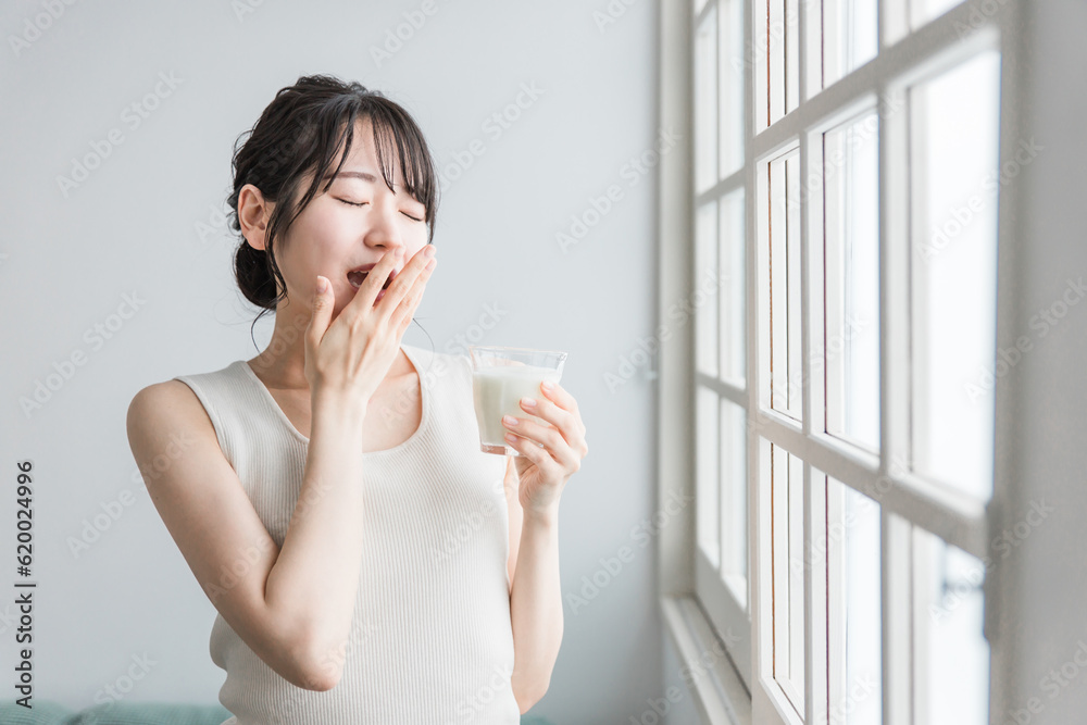 ミルク・牛乳を飲むあくびをする眠いアジア人女性
