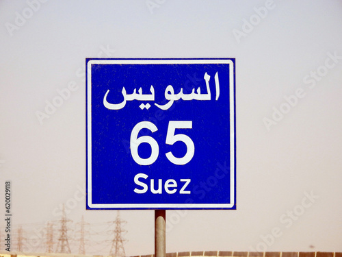 A road sign board in Suez Cairo highway gives the remaining distance to Suez city 65 KM sixty five kilometers written in English and word Suez written in Arabic and English at the side of the street photo