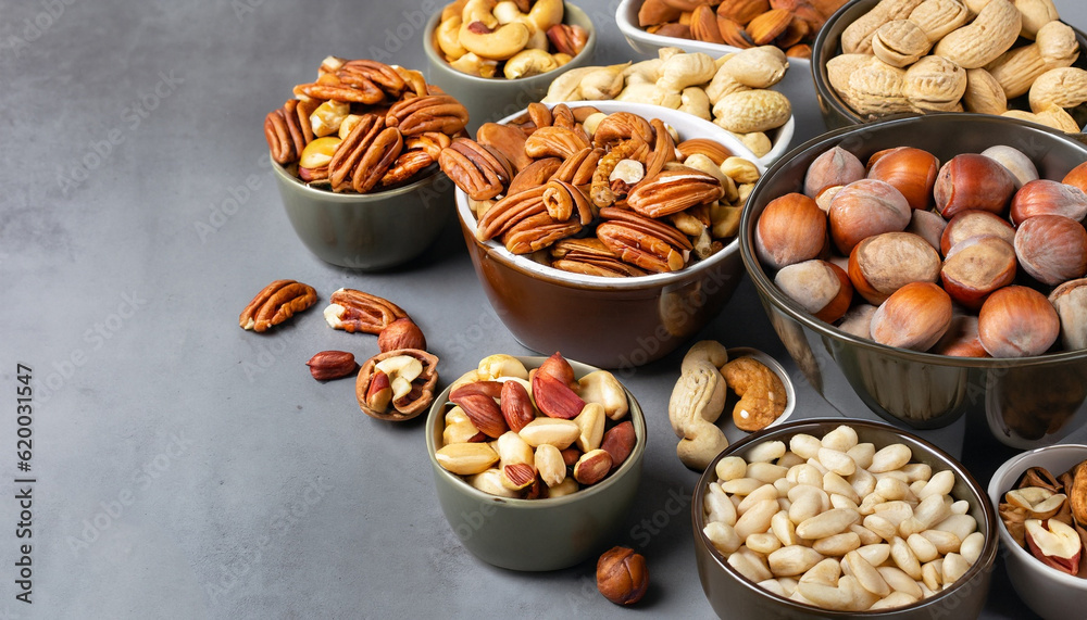 Assortment of nuts in bowls. Cashews, hazelnuts, walnuts, pistachios, pecans, pine nuts, peanuts, macadamia, almonds, brazil nuts. Food mix on gray background, copy space banner