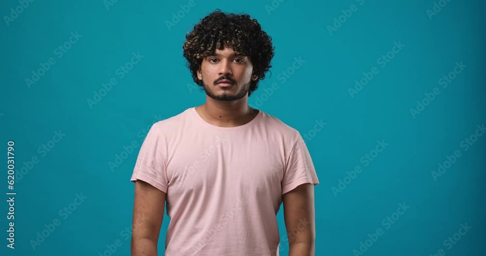 Young serious calm indian man standing isolated over blue studio background Young serious calm indian man standing isolated over blue studio background