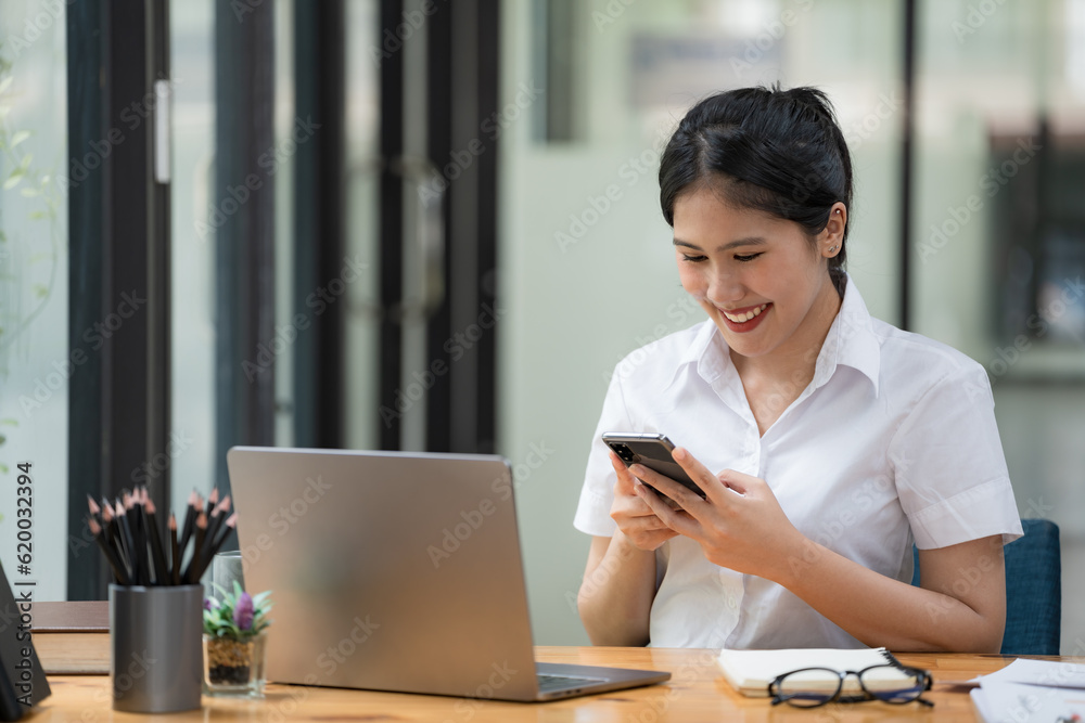 A young Asian businesswoman holding a mobile phone while sitting at her working place in the office. A young Asian businesswoman holding a mobile phone while sitting at her working place in the office.