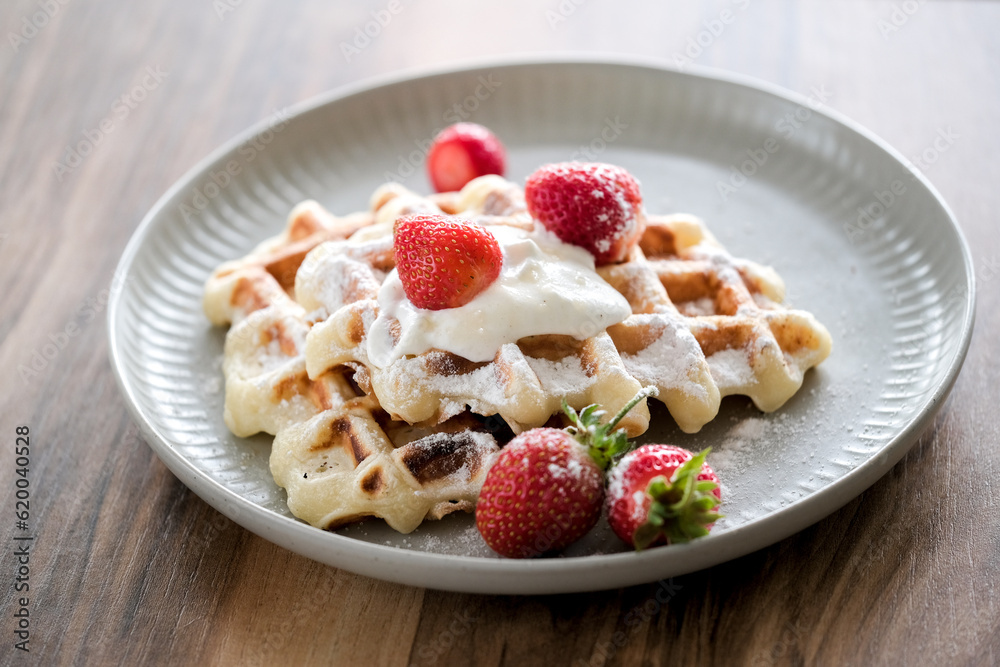 Belgian waffles with strawberry and powdered sugar on plate, wooden table background Belgian waffles with strawberry and powdered sugar on plate, wooden table background