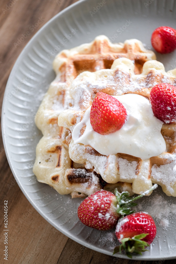 Belgian waffles with strawberry and powdered sugar on plate, wooden table background