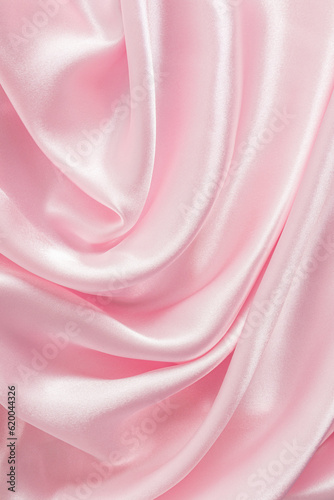 The delicate texture of the waves of pink silk satin fabric. Vertical abstract festive fabric background. background image, layout.