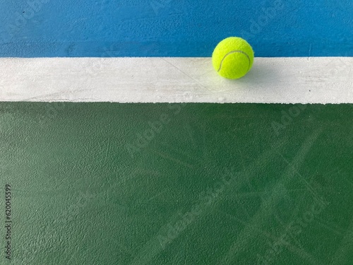 the green tennis ball is at the end of the white backline of a blue-green tennis court in daylight