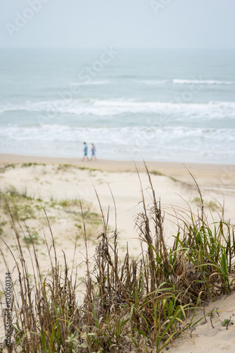 Two people walking on beach with sand dunes