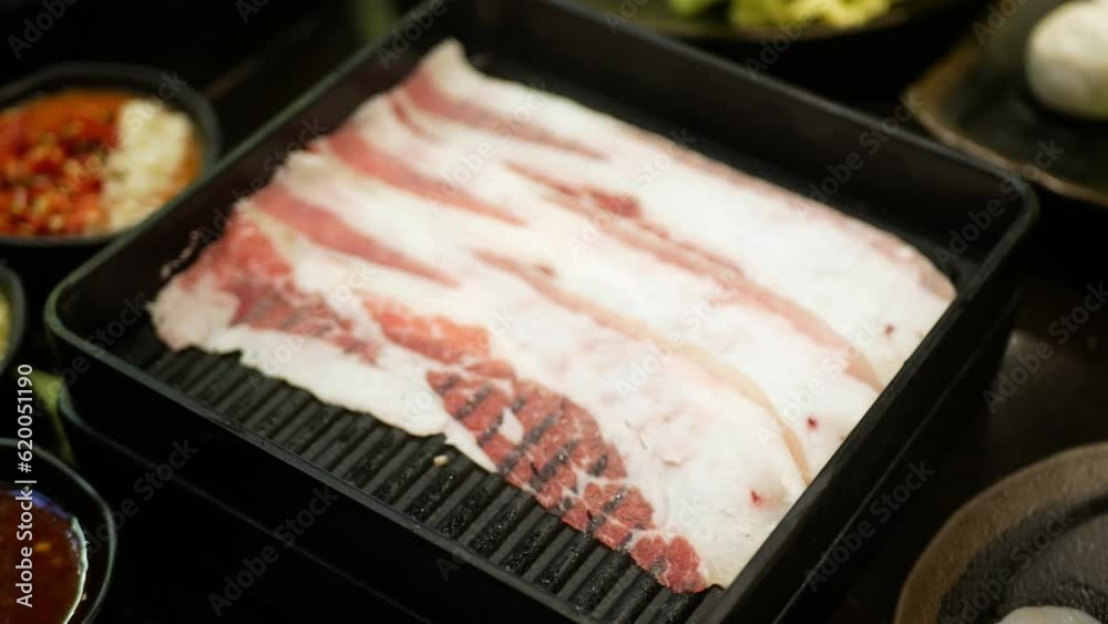 selective focusing close up to tray of beef slice while using chopstick pickup ingredient a piece of raw beef sliced from tray to cook in shabu hotpot japanese food style.
