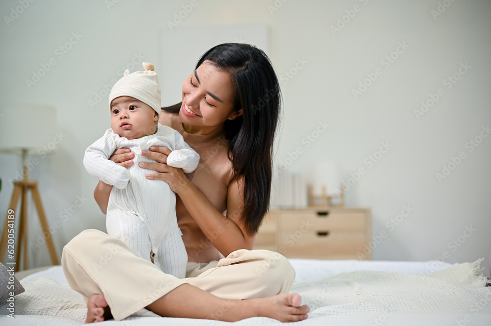 Young beautiful Asian mother holding her baby boy in her arms while sitting on bed. Young beautiful Asian mother holding her baby boy in her arms while sitting on bed.