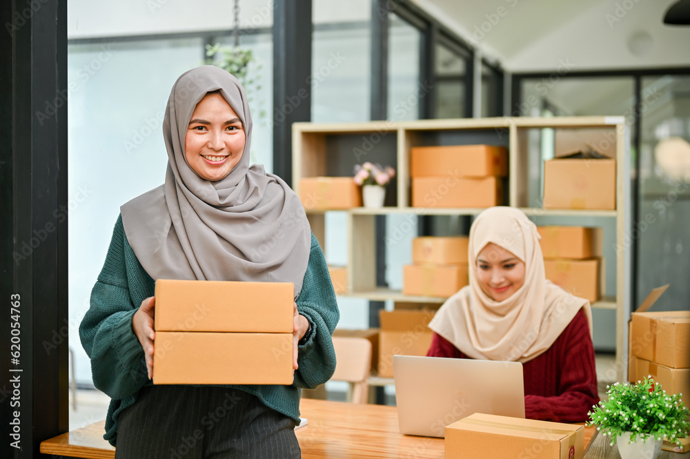 A happy young Asian Muslim female online seller working with her employee in the office. A happy young Asian Muslim female online seller working with her employee in the office.