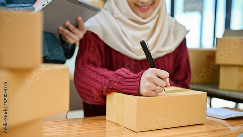 Young Muslim online business owner writing customer's address on the box. close-up image