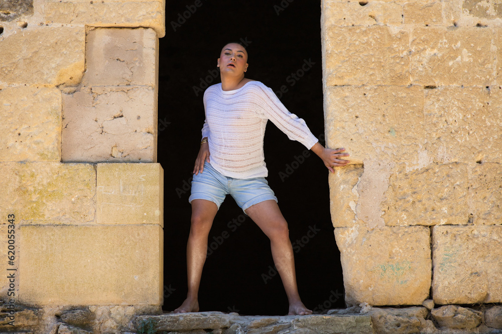 Non binary latin and young person, is in a castle making different body expressions in the hole of the door. Concept of diversity, homosexuality and gay pride.