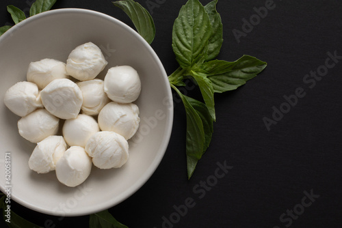 Top view closeup of a bowl with fresh mozzarella and basil leaves on black background with a copy space