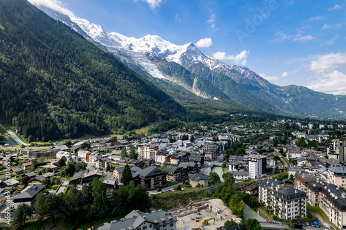 Aerial of Chamonix village at the feet of the Mont Blanc Massive mountain range with eternal snow tops in the background during summer. Tourist destination and outdoor winter sports ski resort.