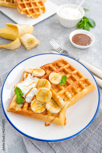 Waffles with banana, whipped cream and salty caramel on a gray concrete background.