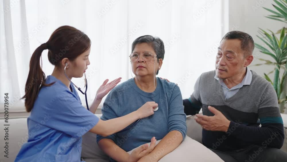Asian female nurse caregiver using stethoscope checking heartbeat and lungs of mature middle aged woman patient. Nursing service and elderly people cardiology healthcare. Elderly care concept Asian female nurse caregiver using stethoscope checking heartbeat and lungs of mature middle aged woman patient. Nursing service and elderly people cardiology healthcare. Elderly care concept