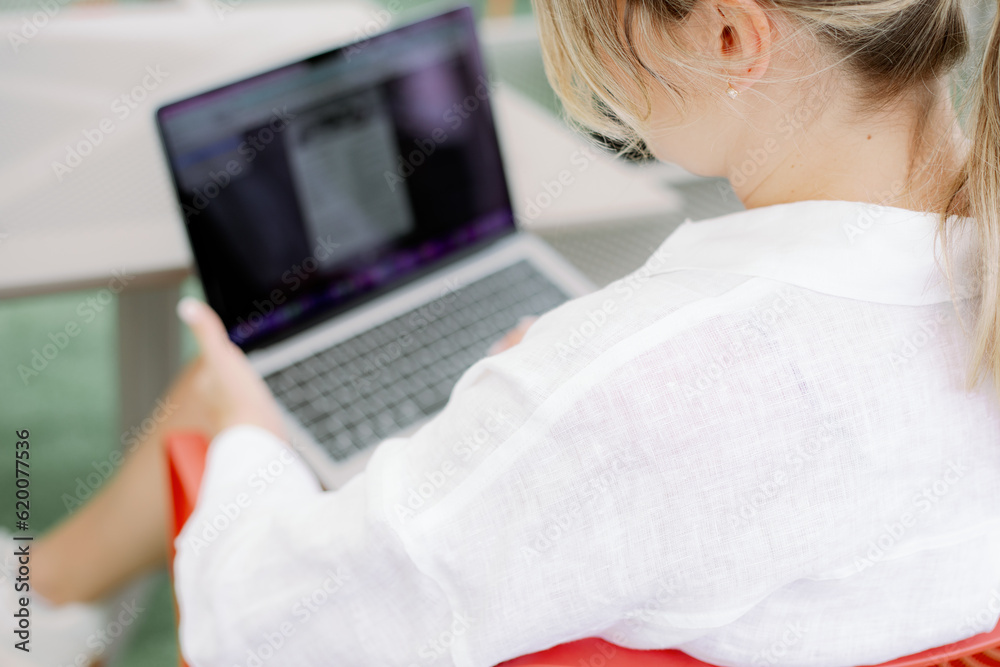 Rear view of seated on chair at table woman in white shirt holding laptop on lap, looking at monitor and freelancing. Rear view of seated on chair at table woman in white shirt holding laptop on lap, looking at monitor and freelancing.