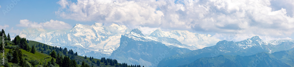 Wide panorama of Mont Blanc Massive eternal snow tops in atmospheric haze with dramatic clouds rising above seen from Col de Joux Plane