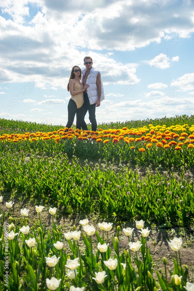 A beautiful young couple, fashion models stands in sportswear at the background of a field of colorful tulips.