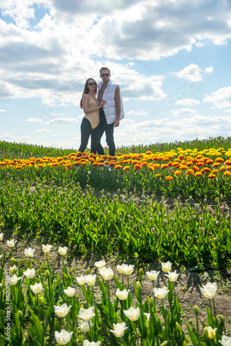 Obraz na płótnie A beautiful young couple, fashion models stands in sportswear at the background of a field of colorful tulips. w salonie