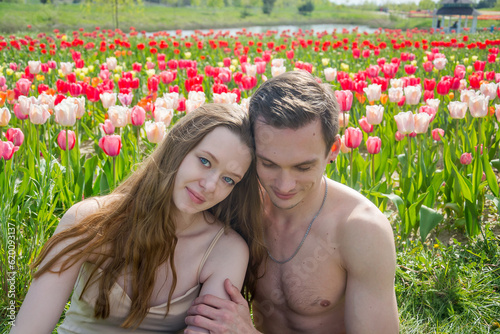 Obraz na płótnie Young beautiful smiling couple sits on the background of a field of colorful tulips. w salonie
