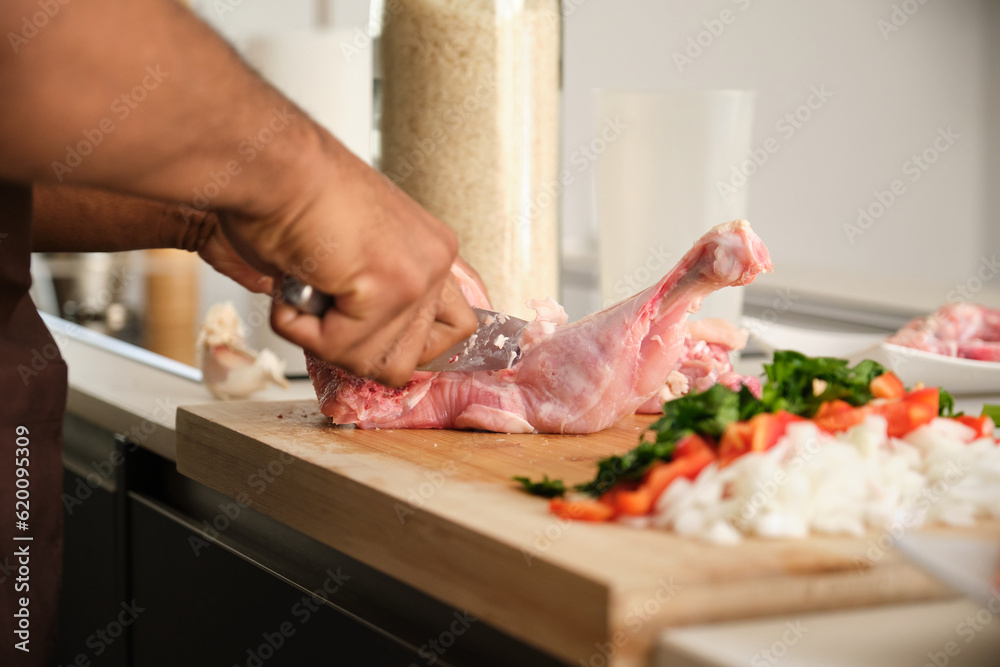 Unrecognizable young black man de-boning chicken to prepare a recipe in a kitchen.