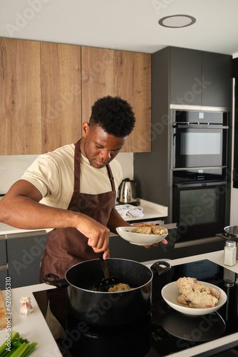 Young black man preparing fried chicken mince with vegetables recipe in a kitchen.