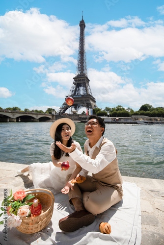 Asian smiling couple having a picnic near the Eiffel tower and the Seine river.
