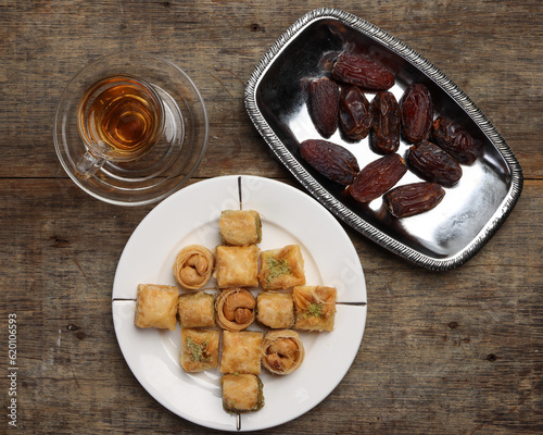 Layered stuffed pastry Baklava middle eastern sweet dessert dry ripe sweet date fruit tea in transparent glass cup saucer on rustic wooden background photo