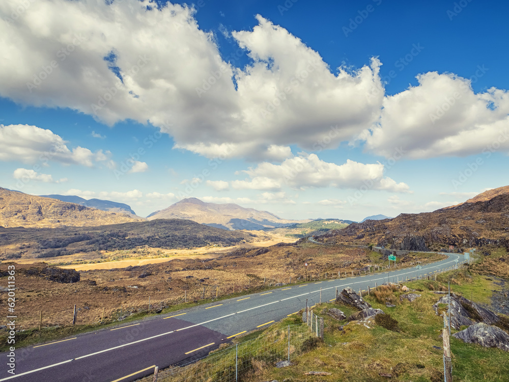 Small asphalt road with stunning nature scenery in county Kerry, Ireland. Amazing Irish landscape by a popular travel rout for tourist. Warm sunny day cloudy sky. Sightseeing and explore wild scenery
