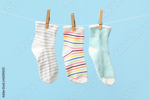 Different socks hanging on rope against color background