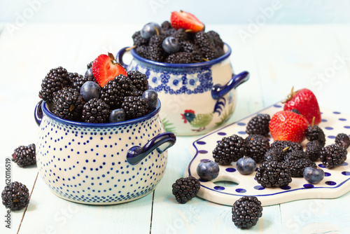 Fresh blackberries and strawberries in ceramic soup bowls on the table. Selective focus.  photo