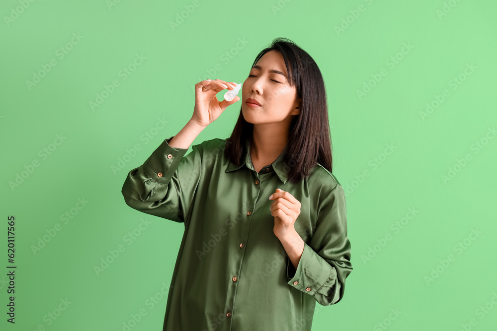 Allergic Asian woman with nasal drops on green background Allergic Asian woman with nasal drops on green background