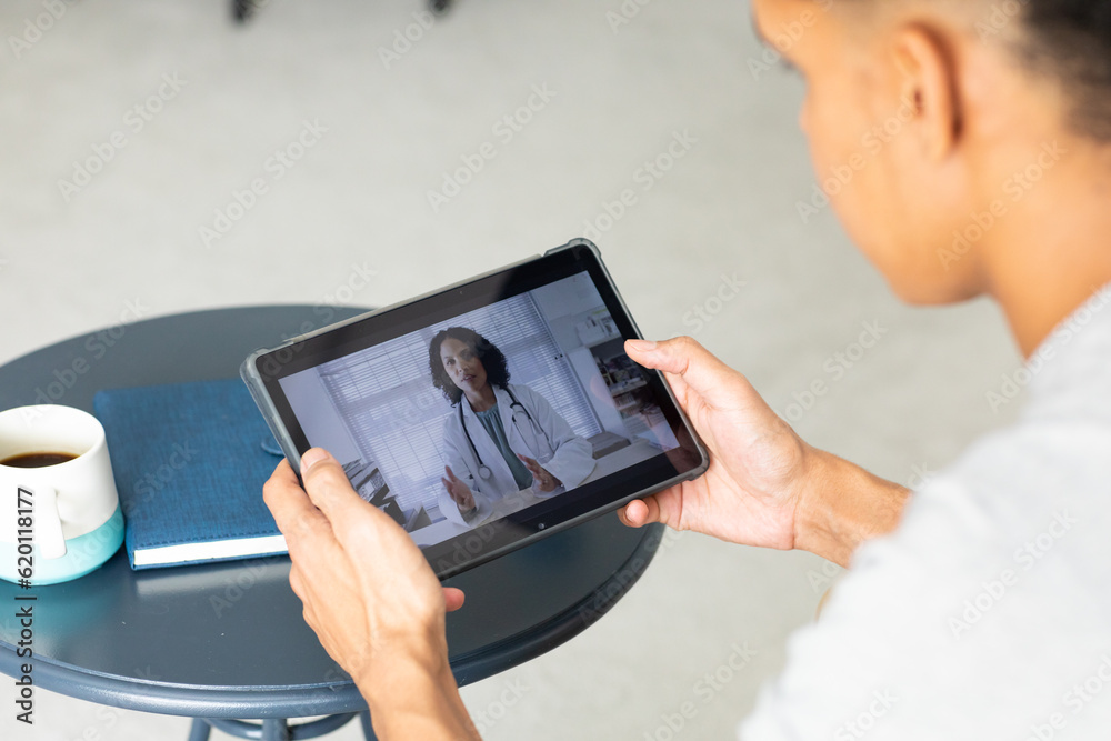 Close up of biracial man using tablet for consultation video call with biracial female doctor