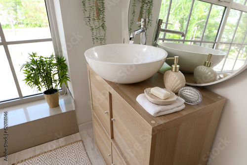 Sink bowl, soap bar and dispenser on wooden cabinet in bathroom